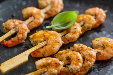 Shrimps on skewer with spices and herbs served on dark plate. Closeup. 