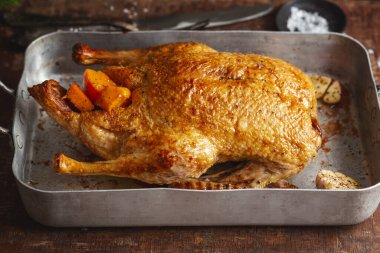 Baked roasted duck with vegetables on pan on old wooden background. Closeup