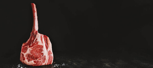 Fresh meat tomahawk steak on old wooden board. Dark background. Horizontal. Banner