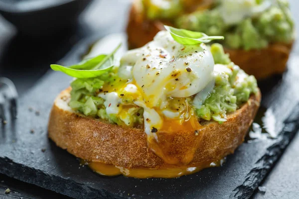 Tasty appetizing toast with avocado and egg served on dark board.