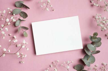 Düğün davetiyesi ya da tebrik kartı maketi, okaliptüs ve çigila çiçekleri kağıda dökülmüş düz uzanmış..