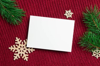 Noel tebrik kartı modeli, ahşap kar taneleri süslemeleri ve kırmızı örülmüş arka planda çam ağacı dalları.