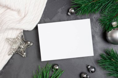 Gümüş renkli şenlik süsleri ve koyu arkaplanda çam ağacı dalları olan Noel tebrik kartı modeli.