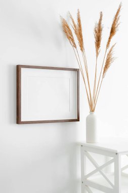 Resim, fotoğraf, baskı ve resim sunumu için yatay ahşap çerçeve modeli. Vazo ve kuru çim dekorasyonlu beyaz duvar. Minimalist iç tasarım.