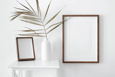 Resim, fotoğraf ya da baskı sunumu için beyaz duvara iki portre ahşap pasaport çerçevesi. Vazo ve palmiye yapraklı minimalist iç tasarım.