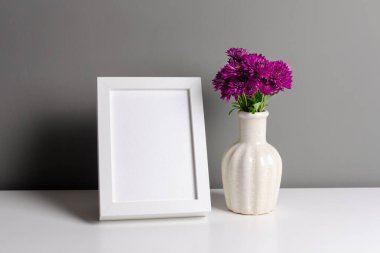 Resim, fotoğraf ve baskı sunumu için beyaz çerçeve modeli. Gri duvar içi vazoda taze kasımpatı çiçekleri var..