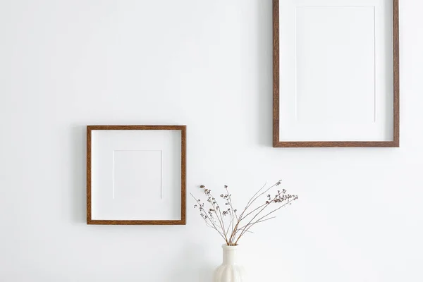 Resim, baskı veya fotoğraf sunumu için çerçeve modelleri. Beyaz duvarda boş ahşap çerçeveler ve kuru bitki süslemeleri. Minimalist iç tasarım.