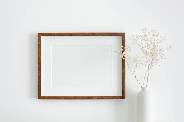 Eserler, fotoğraf ya da baskı sunumu için fotokopi alanı olan tahta çerçeve modeli. Beyaz duvar ve vazo, kuru çingene çiçeği süslemeli. Minimalistik iç tasarım.