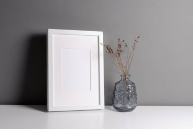 Resim, fotoğraf ve baskı sunumu için beyaz çerçeve modeli. Kuru bitki süslemeleri ile gri duvar iç mimarisi.