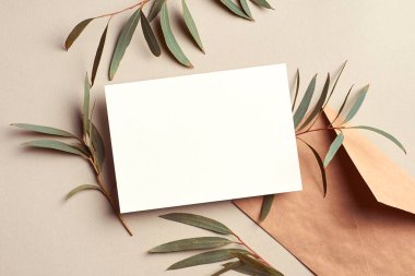 Invitation or greeting card mockup with envelope and fresh eucalyptus twigs, stylish top view mockup with copy space