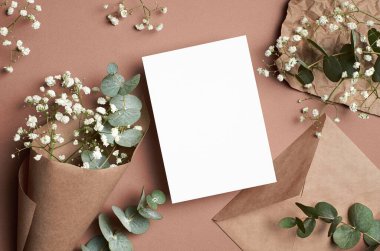 Wedding invitation or greeting card mockup with envelope, eucalyptus and gypsophila flowers on beige paper background