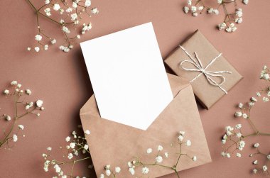 Greeting card mockup, flat lay with gift box, envelope and white gypsophila flowers decorations on paper background. Card mockup with copy space.