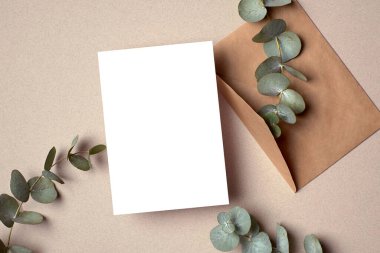 Greeting or invitation card mockup with envelope and natural eucalyptus twigs. Blank card with copy space.