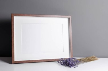 Landscape wooden frame mockup for artwork, photo and print presentation on white table over grey wall, dry lavender flowers.