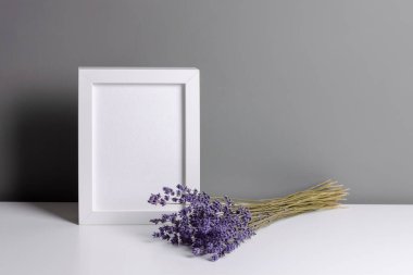 Portrait white frame mockup for artwork, photo and print presentation. Grey walll interior with dry lavender flowers bouquet.