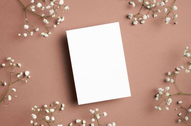 Wedding invitation or greeting card mockup with white gypsophila flower on beige paper background. Top view with copy space.