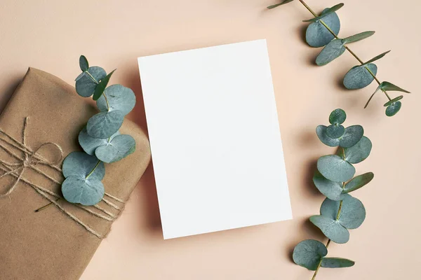 Greeting card mockup with gift box and natural eucalyptus twigs on paper background. Card mockup with copy space.