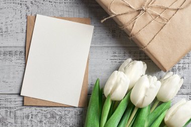 Tebrik kartı modeli hediye kutusu ve ahşap arka planda beyaz lale çiçekleri.