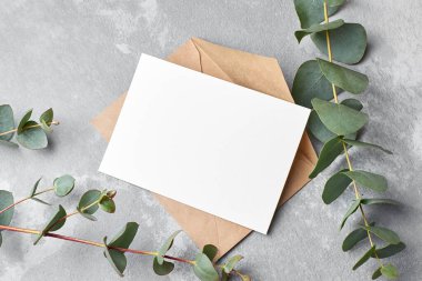 Invitation or greeting card mockup with fresh eucalyptus twigs on grey concrete background, copy space, top view