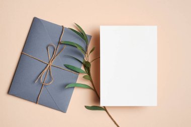 Invitation or greeting card mockup with envelope and natural eucalyptus twig on paper background. Blank card with copy space.