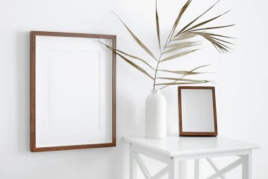 Boş portre çerçeveleri beyaz duvarda mobilya ve vazoda kuru palmiye yaprağı süslemeleri. Minimalistik İskandinav tarzı iç mimari modeli.