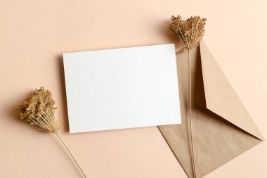 Bej arkaplan, üst görünüm, kopyalama alanı üzerinde zarf ve kuru bitki süslemeleri içeren davetiye veya tebrik kartı maketi