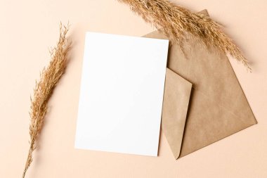 Bej arkaplan, üst görünüm, kopyalama alanı üzerinde zarf ve kuru bitki süslemeleri içeren davetiye veya tebrik kartı maketi