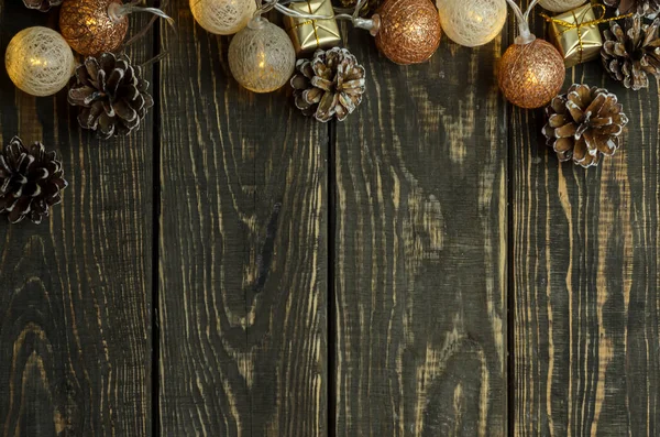 Темный деревянный фон с рождественской гирляндой и шишками. — стоковое фото