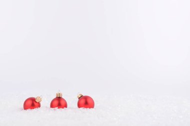 Beyaz arka planda karda üç kırmızı Noel topu.. 