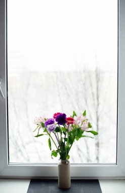 A bright delicate bouquet of flowers on the background of a white winter window.