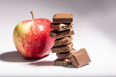 Ön planda kahverengi gözenekli çikolata beyaz bir masada bir elmanın arka planında.