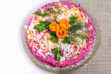 Herring salad under a fur coat on a glass dish with carrot flowers.