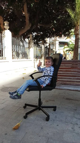 Şehir sokaklarında ofis sandalyesinde oturan bir çocuk.