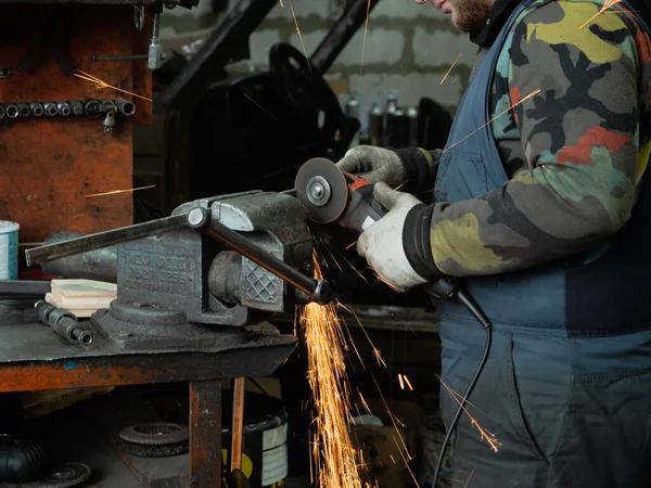 Sakallı bir adamın ellerinde öğütme makinesi, her yöne doğru parlak kıvılcımlar uçuşuyor..