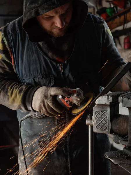 Sakallı bir adamın ellerinde öğütme makinesi, her yöne doğru parlak kıvılcımlar uçuşuyor..
