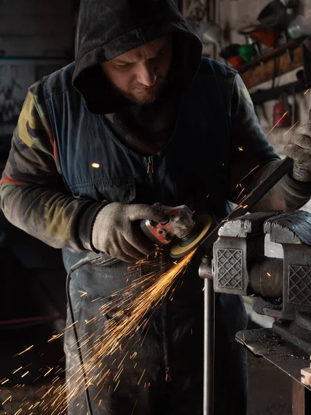 Sakallı bir adamın ellerinde öğütme makinesi, her yöne doğru parlak kıvılcımlar uçuşuyor..