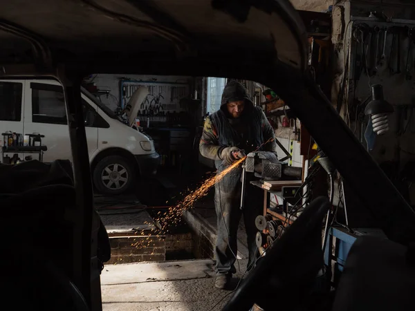 Sakallı bir adamın ellerinde öğütme makinesi, her yöne doğru parlak kıvılcımlar uçuşuyor..