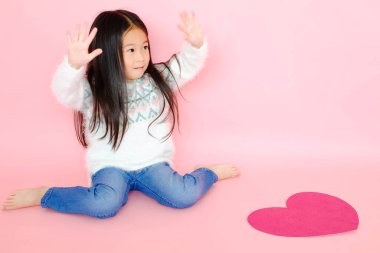 Pembe arka planda güzel bir Asyalı kız çocuğu portresi, kırmızı kalp işareti, aşk konseptinde sevgililer günü.