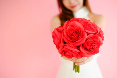 Pembe arka planda, elinde kırmızı çiçek buketiyle güzel Asyalı kadın portresi, aşk konseptinde mutlu sevgililer günü.