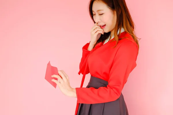 手に持っている赤い封筒でピンクの背景に赤い韓服韓国スタイルを身に着けている肖像美しいアジアの女性は 中国の新年のコンセプトを祝う — ストック写真