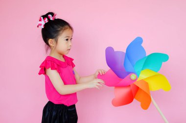 Renkli rüzgar türbini, fırıldak ya da rüzgar oyuncağı olan pembe arka planda küçük tatlı Asyalı kız.