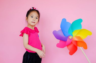 Renkli rüzgar türbini, fırıldak ya da rüzgar oyuncağı olan pembe arka planda küçük tatlı Asyalı kız.