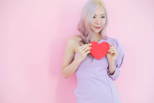ピンクの背景に肖像美しいアジアの女性 愛のコンセプトで幸せなバレンタインデー 手で赤いハートサインを保持モデル — ストック写真