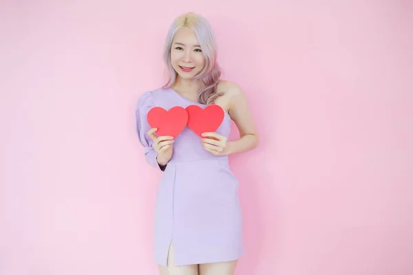 ピンクの背景に肖像美しいアジアの女性 愛のコンセプトで幸せなバレンタインデー 手で赤いハートサインを保持モデル — ストック写真