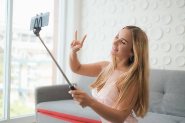Seksi beyaz kadın elinde akıllı telefonuyla selfie çubuğu tutuyor.
