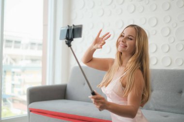 Seksi beyaz kadın elinde akıllı telefonuyla selfie çubuğu tutuyor.