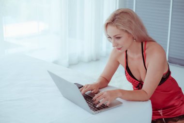 Beyaz kadın sabahları kırmızı pijama giyer ve dizüstü bilgisayarla oynar.