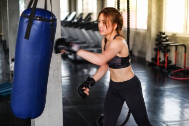 Siyah boks eldivenli, kum torbasını yumruklayan boksör eğitimli çekici bir Asyalı kadın.