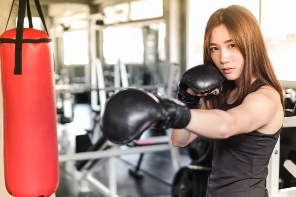 Portrait asian woman with black boxing gloves and red punching bag wearing sportswear in fitness or gym center, Strength sporty female and weight loss concept