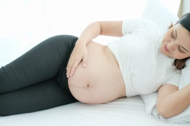 Yatakta yatan genç hamile bir kadının portresi.